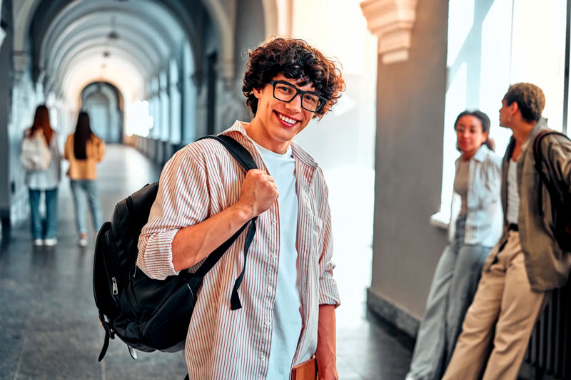 Um grupo de jovens adultos e estudantes, caminhando e conversando em um ambiente urbano ou campus. Eles carregam mochilas e sorriem.
