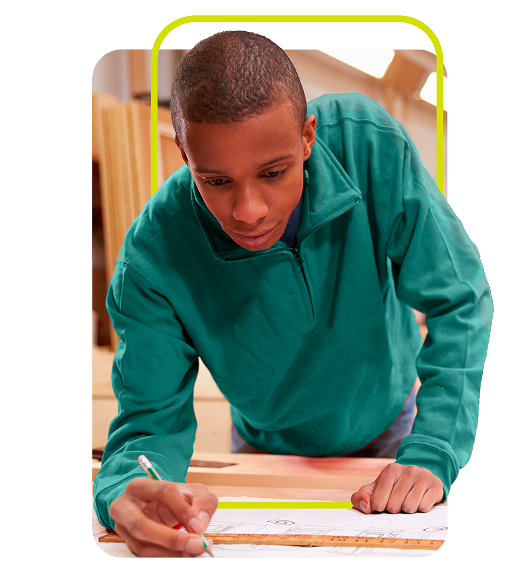 Jovem negro se apoia na mesa enquanto escreve com um lapis em um papel.